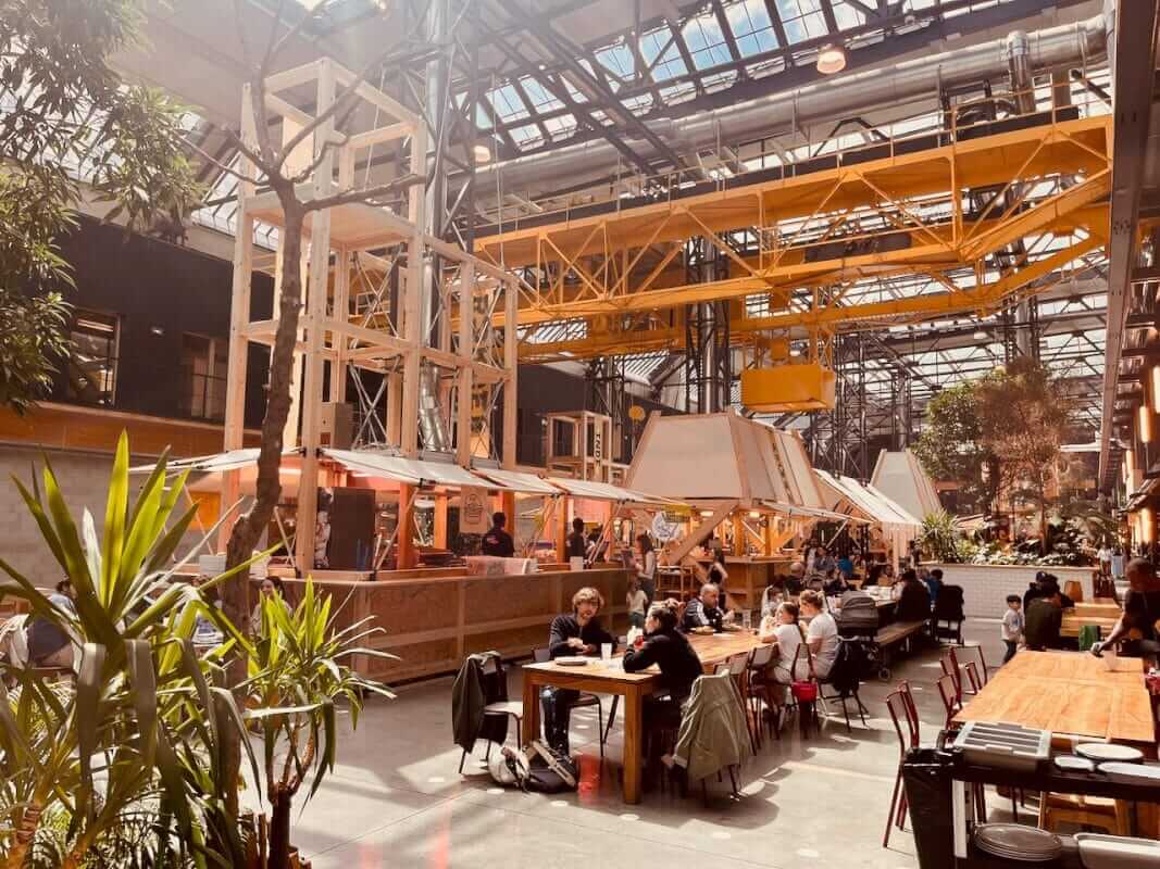 Espace restauration de la Communale Saint-Ouen — charpente bois, plantes et tables sous la verrière